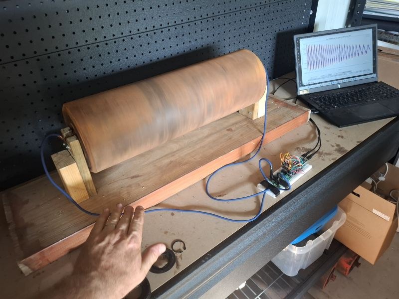 A used conveyor roller on a timber stand with a cable to a breadboard prototype and a laptop showing a coast-down waveform