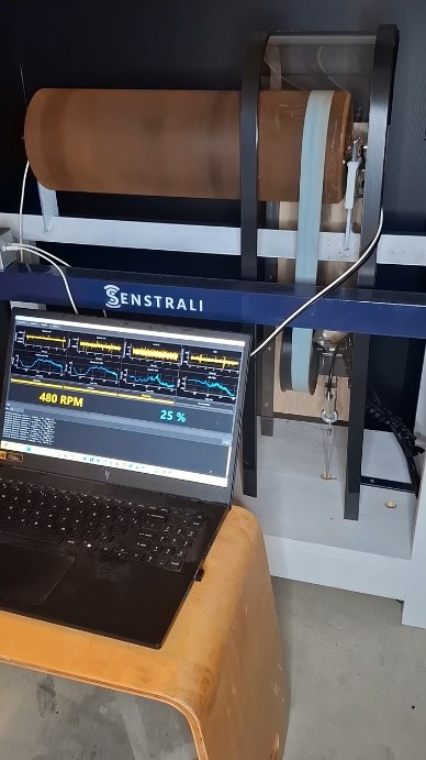 The automated test rig in a Senstrali frame, with a belt-driven roller and a laptop showing speed and load readouts